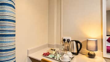 A hotel room with a kitchenette, a kettle, a tray with food items, and a lamp.