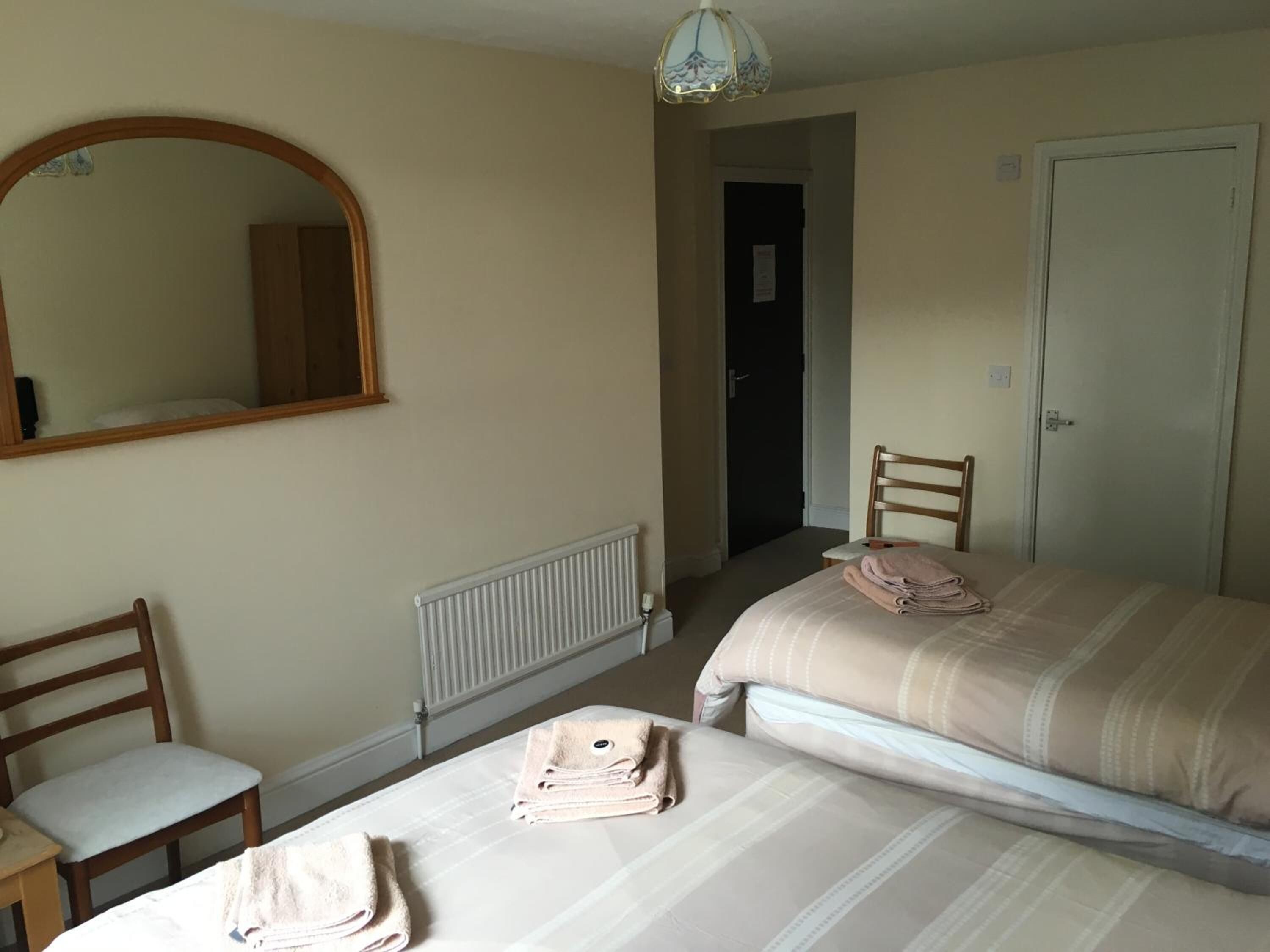 A bedroom with two beds, a chair, a radiator, a mirror, and a door.