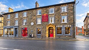 A stone building with a red entrance, a sign for The Hampton Hotel, and a Tanglez shop. - Hampton (Llandrindod Wells)