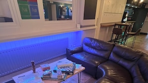 Una sala de estar acogedora con un sofá de cuero, una mesa de centro de madera con juegos de mesa y una pared iluminada en azul.