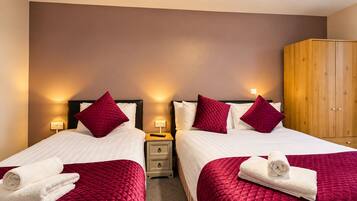 Habitación de hotel con dos camas, cada una con cubrecama rojo acolchado y almohadas blancas, un armario de madera y lámparas de noche.