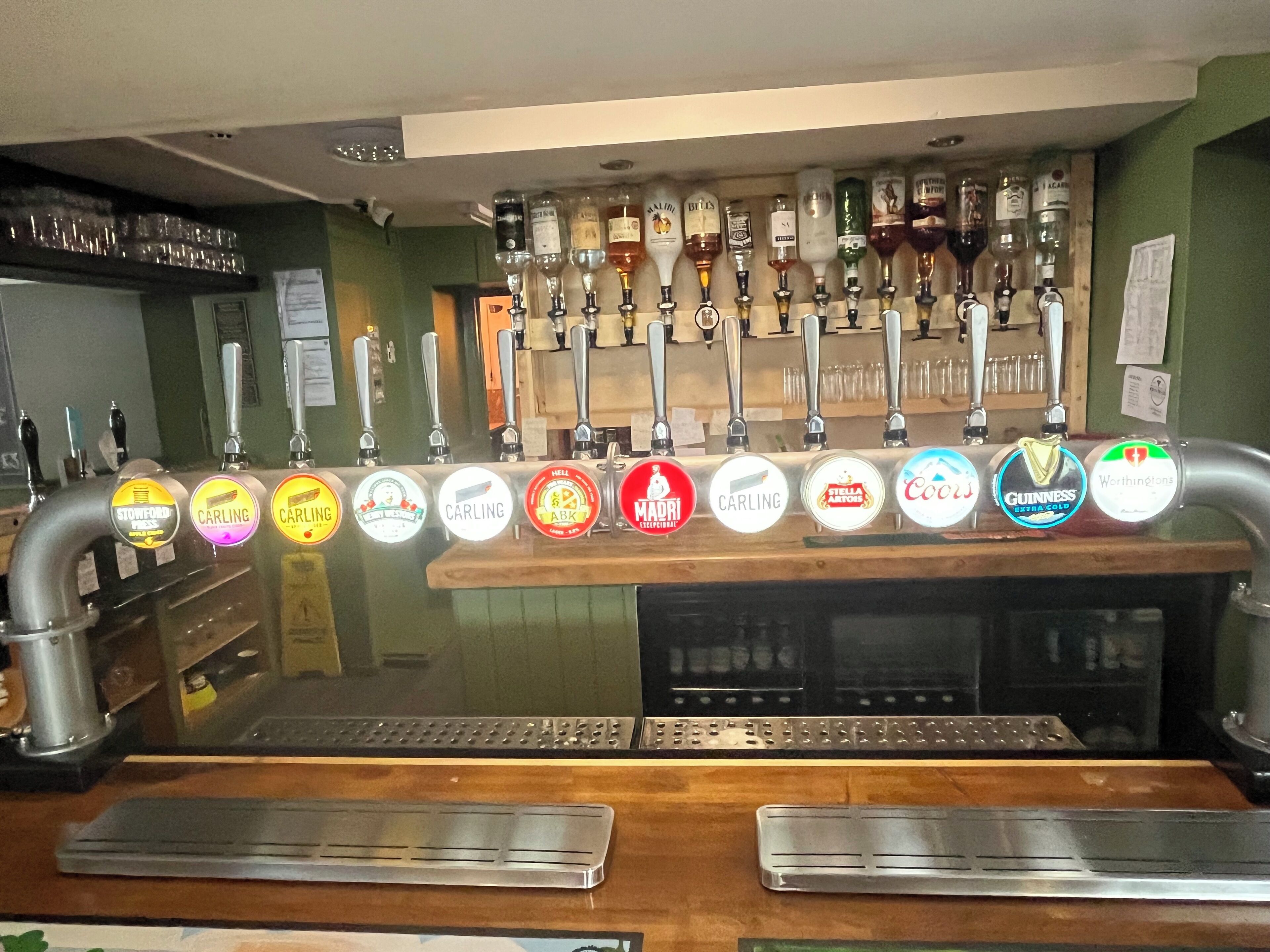 A bar area with a row of beer taps and a selection of bottles on the wall behind.