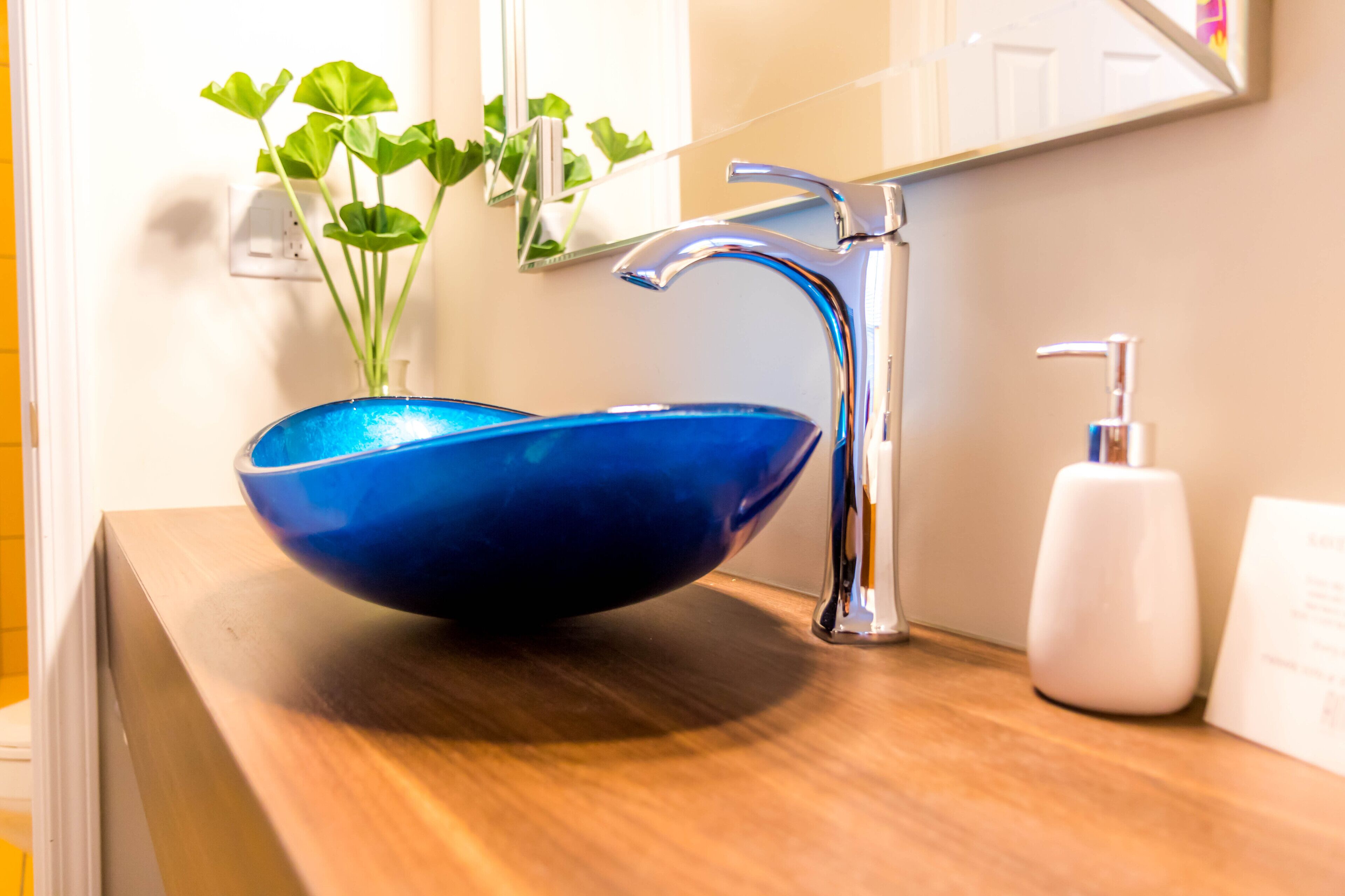 A bathroom with a blue glass bowl sink, a chrome faucet, a white soap dispenser, and a mirror above the sink.