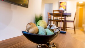 Uma sala de jantar com uma mesa e cadeiras, uma tigela de frutas e uma televisão montada na parede.