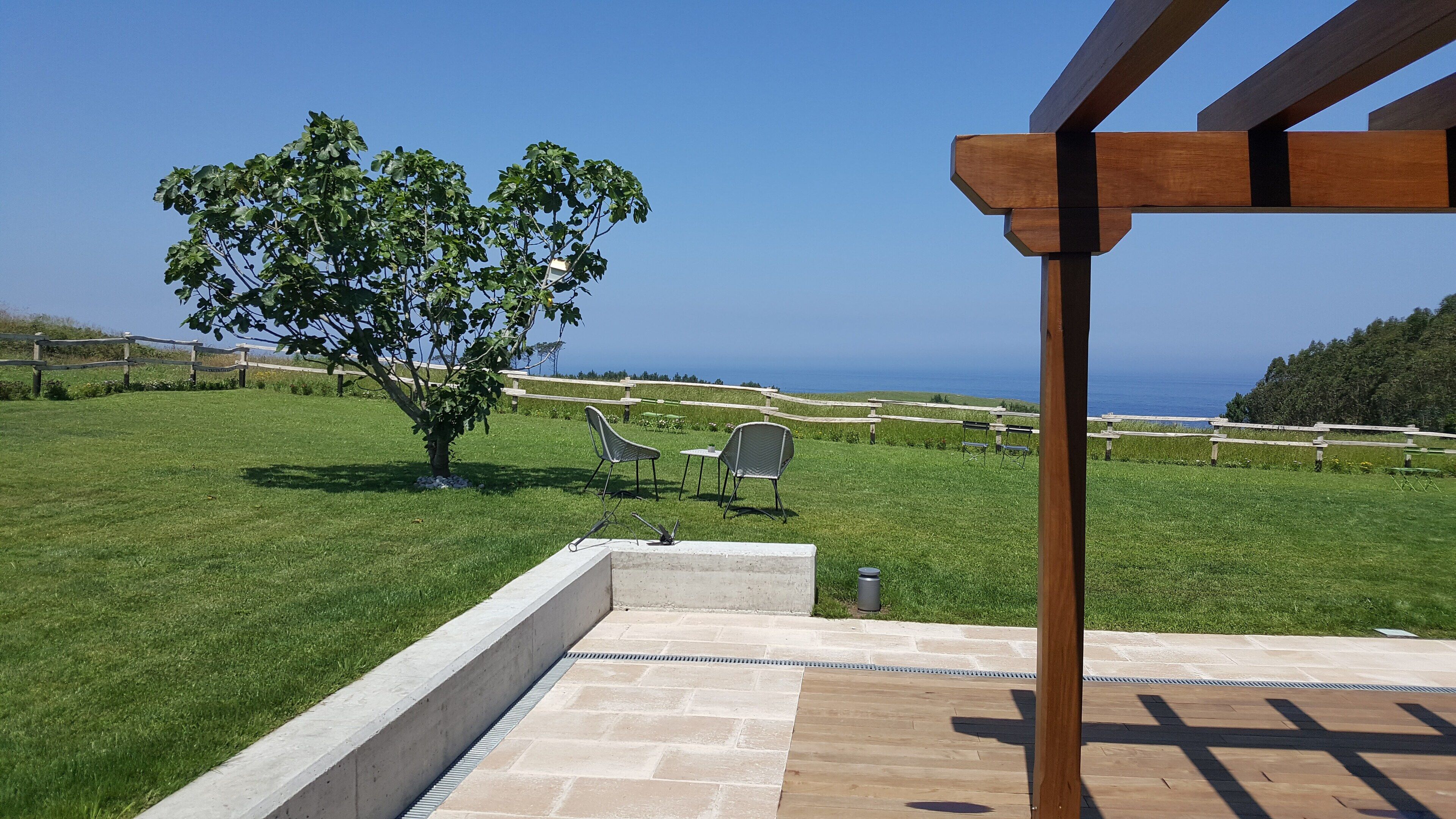 A patio area with a view of the ocean, a tree, and outdoor seating.