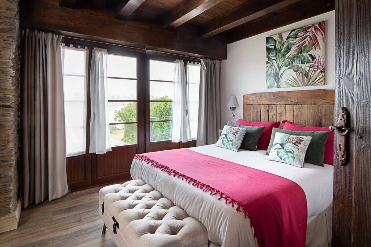 A bedroom with a large bed, wooden headboard, and a view of greenery outside.