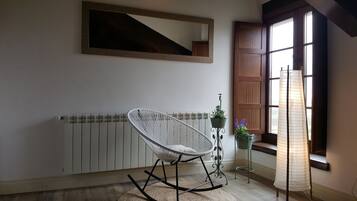 Una habitación con un radiador blanco, una silla de mimbre blanca, una planta en maceta y una ventana con contraventanas de madera.