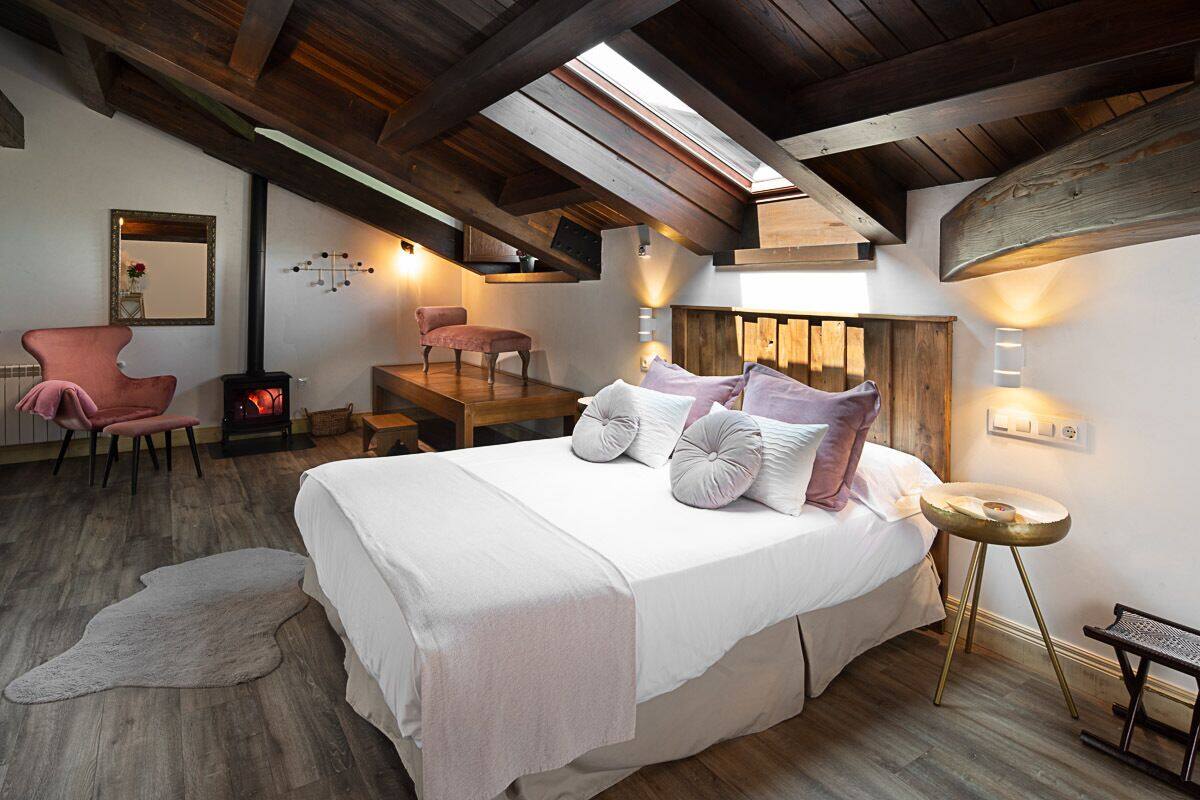 A bedroom with a large bed, a wooden ceiling, a fireplace, and a skylight.