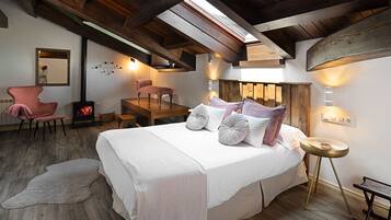 A bedroom with a large bed, a wooden ceiling, a fireplace, and a skylight.