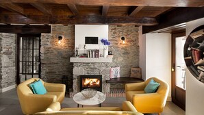 Una sala de estar acogedora con paredes de piedra, chimenea, dos sillones amarillos y una mesa de centro.