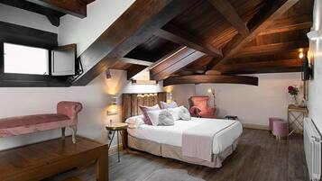 Un dormitorio con techo de madera, una cama con almohadas, un banco, una mesita y un radiador.