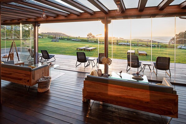 Una amplia terraza exterior con piso de madera, asientos cómodos y una vista panorámica de un campo de golf.