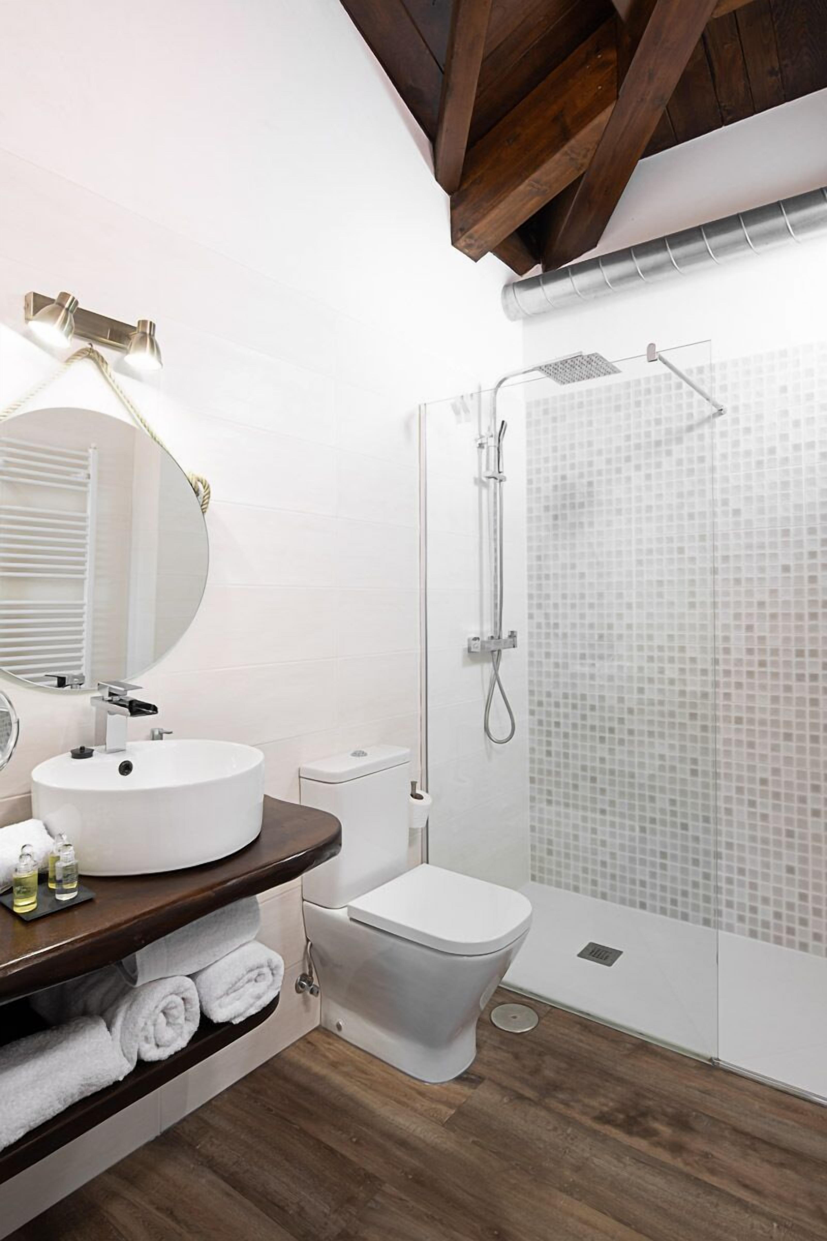 Une salle de bain moderne avec un lavabo rond blanc, un miroir avec un cadre doré, une douche avec une porte en verre et des toilettes.