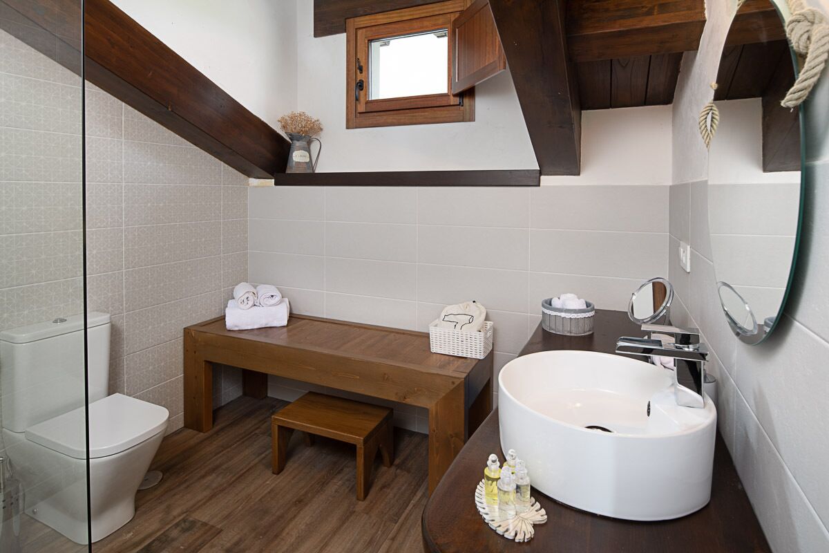 Un baño moderno con un banco de madera, un lavamanos grande y una ventana pequeña sobre el inodoro.