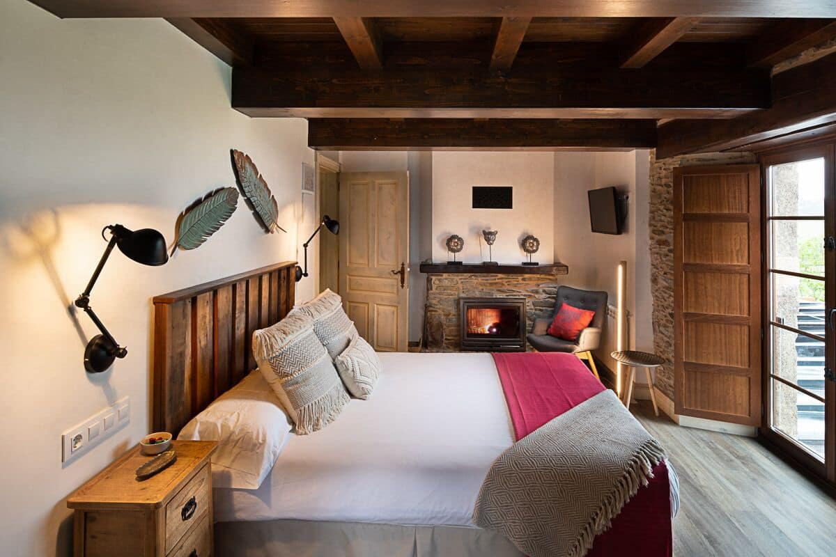 A cozy bedroom with a wooden headboard, a fireplace, and a large window.