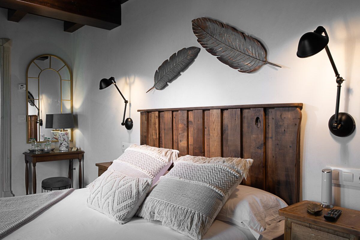 Une chambre à coucher avec une tête de lit en bois, deux grands oreillers, une table de chevet avec une lampe et des décorations en plumes fixées au mur.