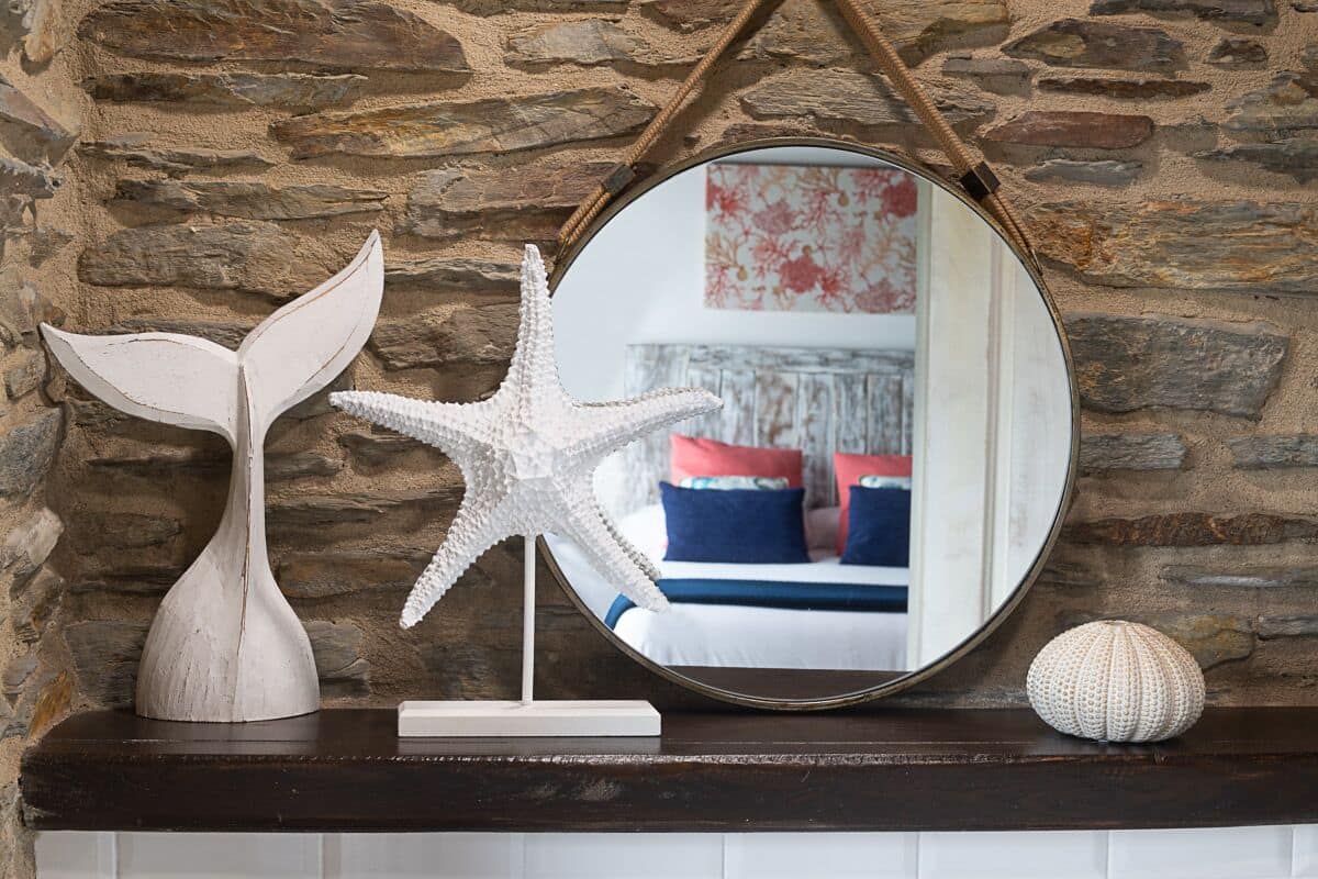 A stone wall with a mirror reflecting a room with blue and red pillows.