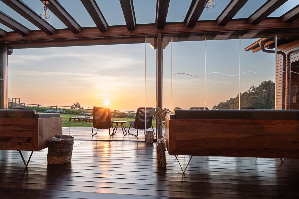 A wooden deck with outdoor seating, large windows, and a view of the sunset.