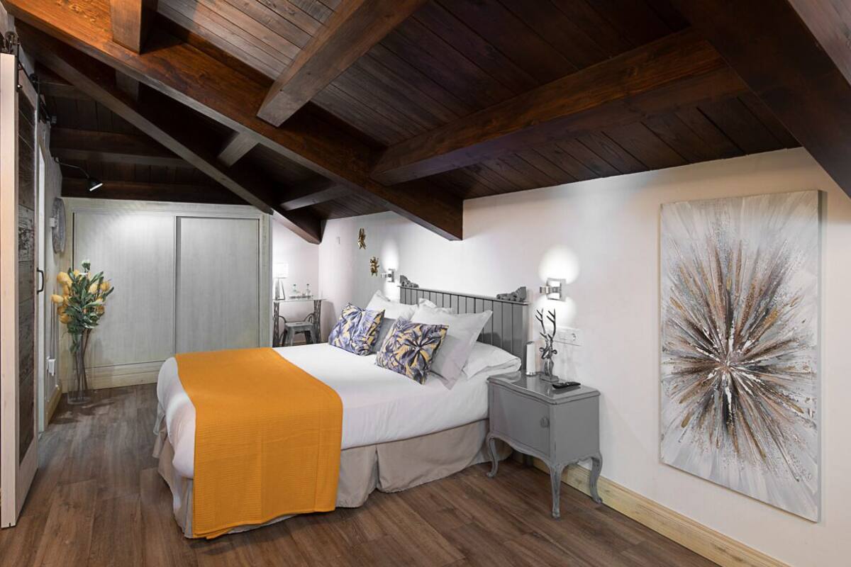 A bedroom with a bed, bedside tables, a nightstand, a wall-mounted artwork, and a wooden ceiling.