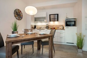 A modern kitchen with white cabinets, a built-in oven, and a microwave. There is a dining table set with plates and glasses.