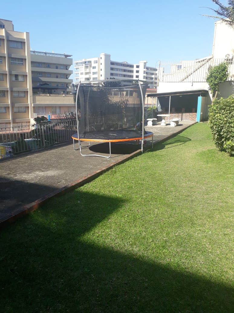 A grassy outdoor area with a trampoline and a covered seating area.