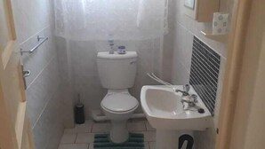A small, tiled bathroom with a toilet, sink, and a green striped rug. - Beach Mansion 1 (Margate)
