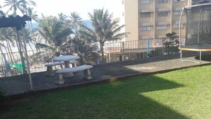 A grassy outdoor area with a tiled patio, a bench, and a playground structure. - Beach Mansion 1 (Margate)