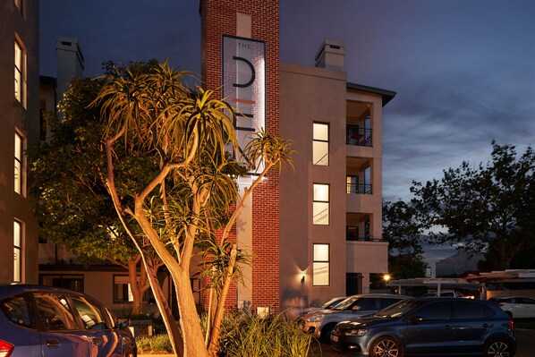 A multi-story building with a prominent 'D' sign on the facade, surrounded by parked cars and palm trees.