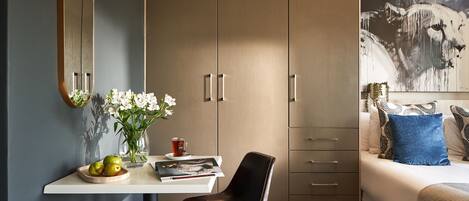 A modern bedroom with a bed, a desk with a chair, a wardrobe, and a large painting on the wall.