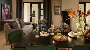 A modern living room with a dining table set for a meal, a sofa, and a TV. - The Den Apartments (Stellenbosch)