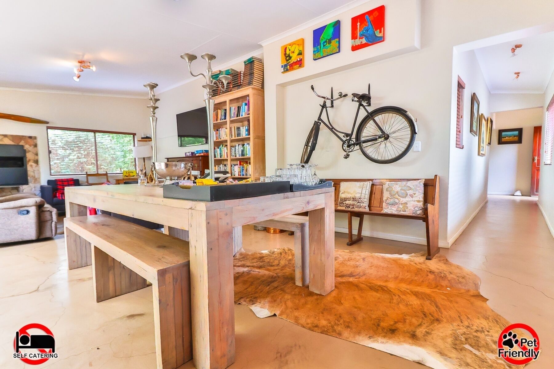 Un salón espacioso con una mesa de madera, una estantería, una bicicleta colgada en la pared y una alfombra de piel.