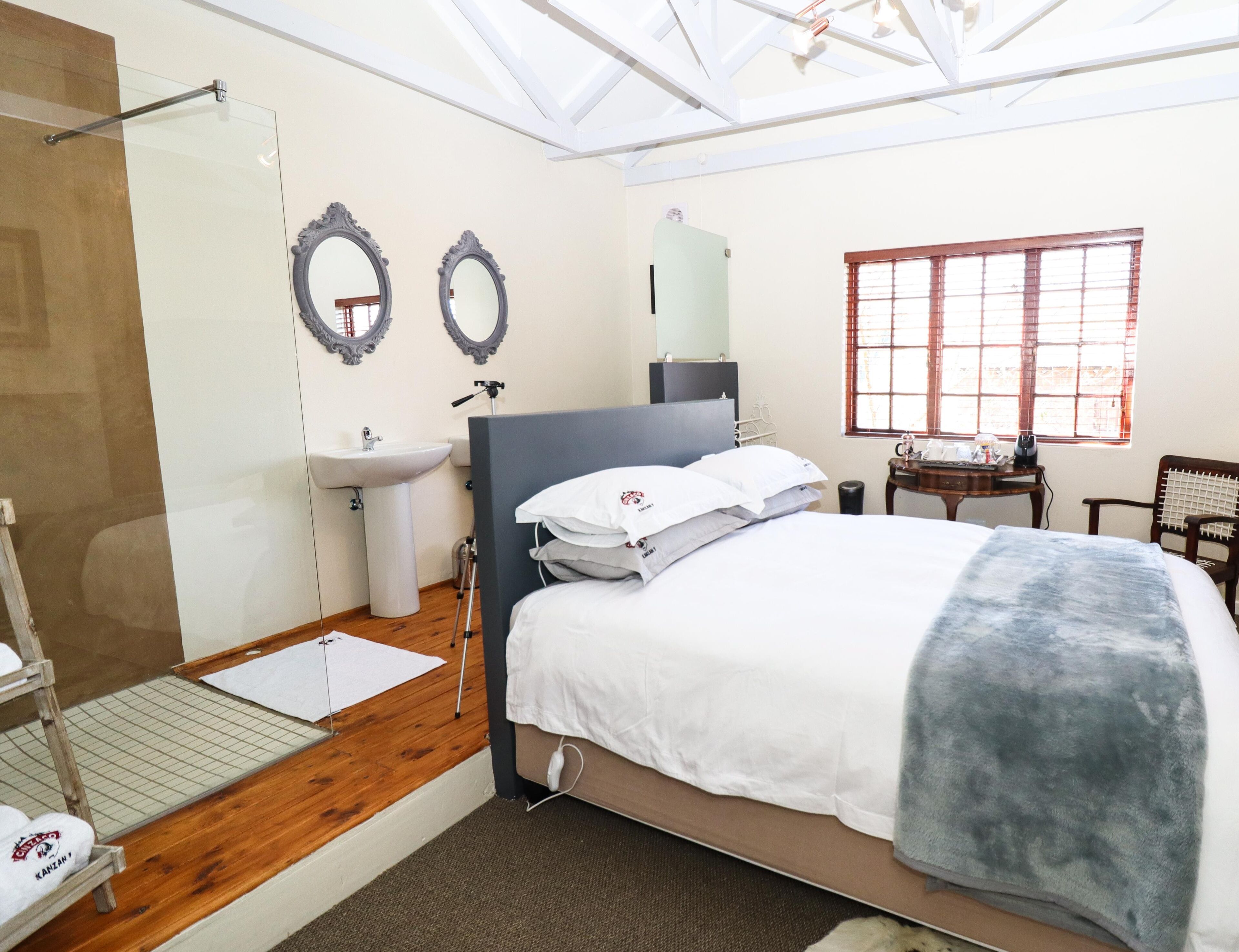 A bedroom with a bed, bedside table, mirror, sink, and window.