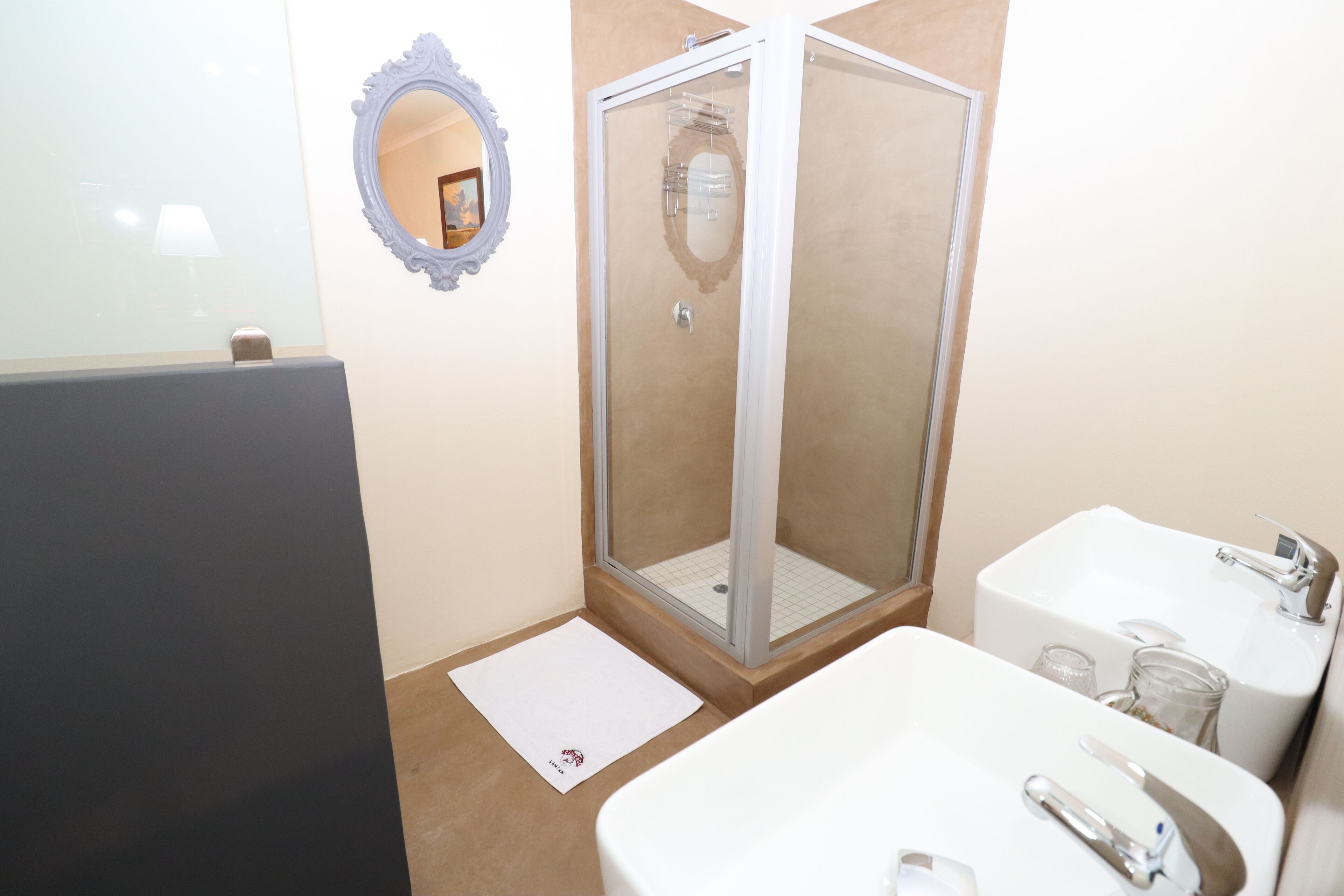 A bathroom with a glass-enclosed shower, a white sink with a mirror, and a small rug on the floor.