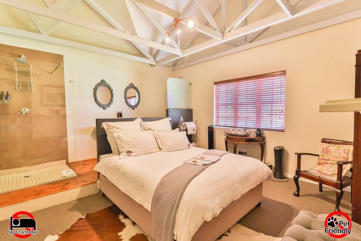 A bedroom with a bed, a shower, a vanity, and a window with blinds.