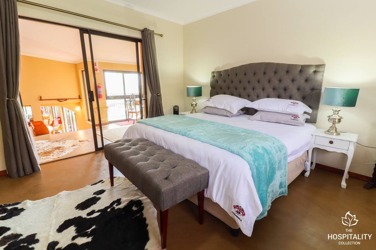 A bedroom with a large bed, a bench, a cowhide rug, and a view of a balcony.