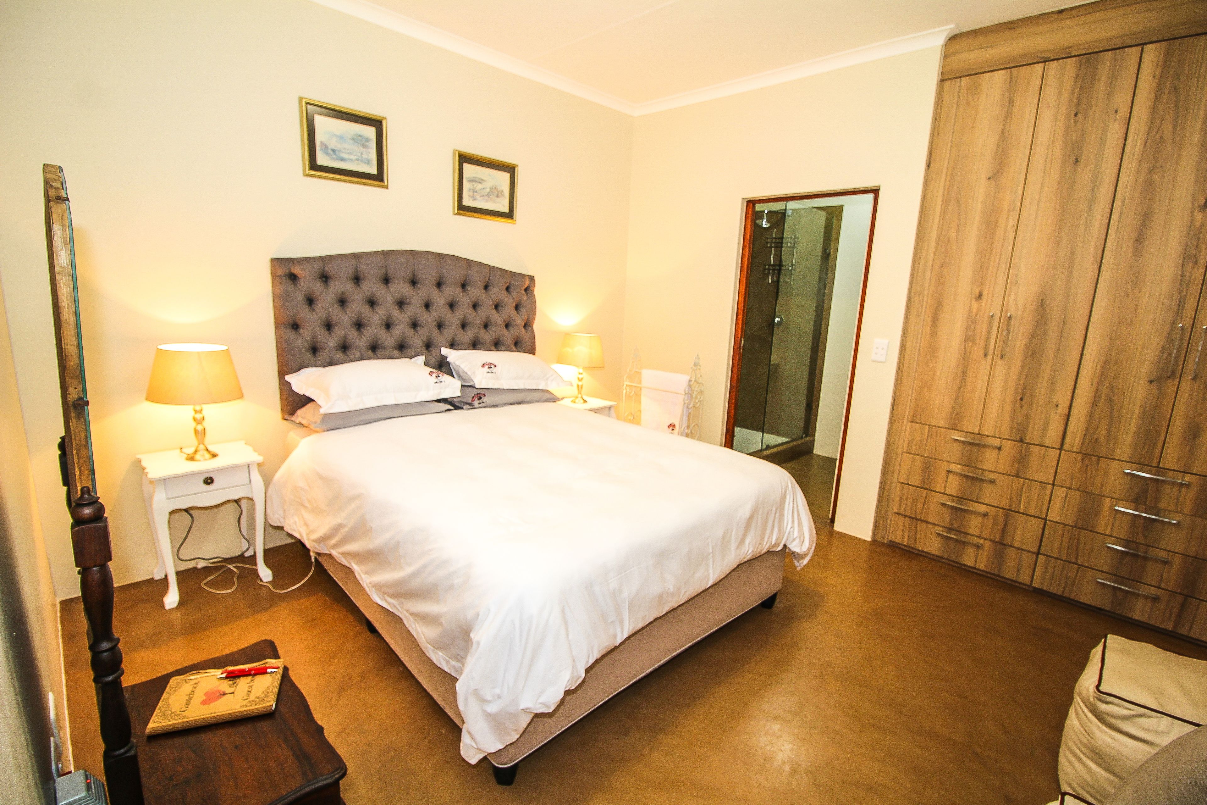 A bedroom with a large bed, two bedside tables with lamps, a wardrobe, and two framed pictures on the wall.