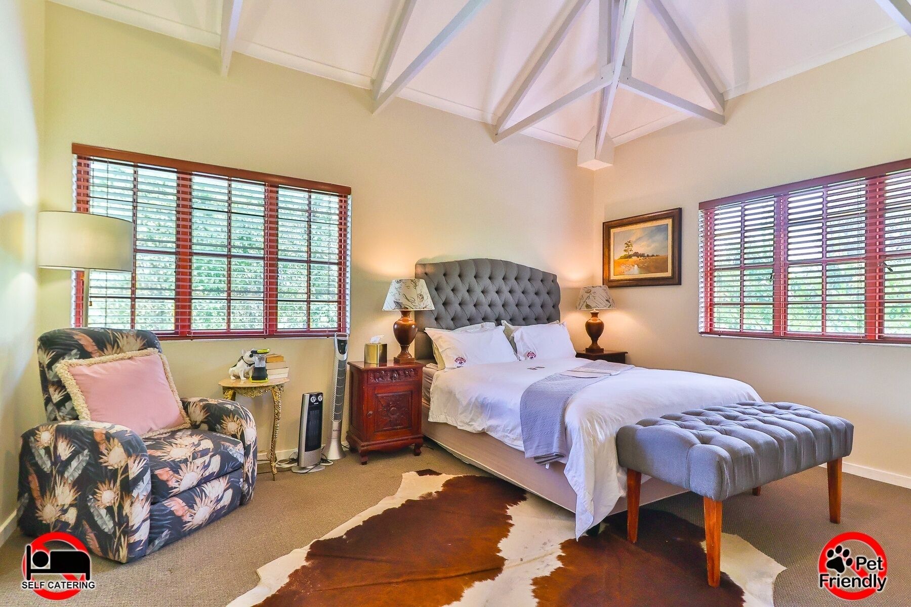 A bedroom with a large bed, two bedside tables, a nightstand, a chair, and a cowhide rug.