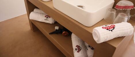 A bathroom with two white sinks, a wooden vanity, and neatly folded towels with a logo.