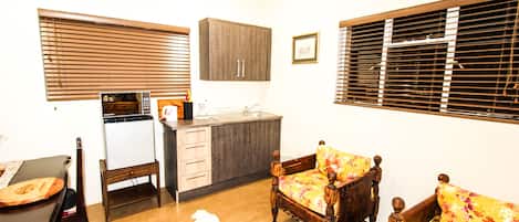 A compact kitchen with a microwave, sink, and wooden cabinets. There is a dining table with chairs and a sofa with floral upholstery.