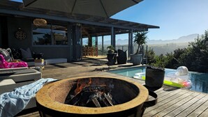 A deck with a fire pit, outdoor seating, and a pool. - Oubaai Villa  (Herolds Bay)