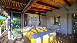 A modern bedroom with a large bed, a glass door leading to a balcony, and a wardrobe with a mirror. - Oubaai Villa  (Herolds Bay)