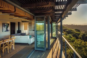 A modern outdoor living space with a wooden deck, a white sofa, and a dining area with wicker chairs. - Oubaai Villa  (Herolds Bay)