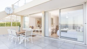 Un espace de vie moderne, à aire ouverte, comprenant une table et des chaises de salle à manger, un canapé et un lit donnant sur l’extérieur grâce à des portes vitrées.