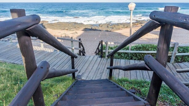 Un escalier en bois menant à une plage d’où l’on a une vue sur l’océan.