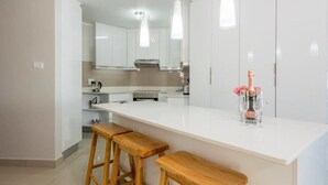 Une cuisine moderne avec des meubles blancs, un plan de travail blanc et des tabourets en bois.