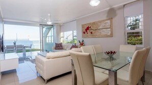 Un salon moderne avec une table à manger en verre, des canapés blancs et un ventilateur de plafond.