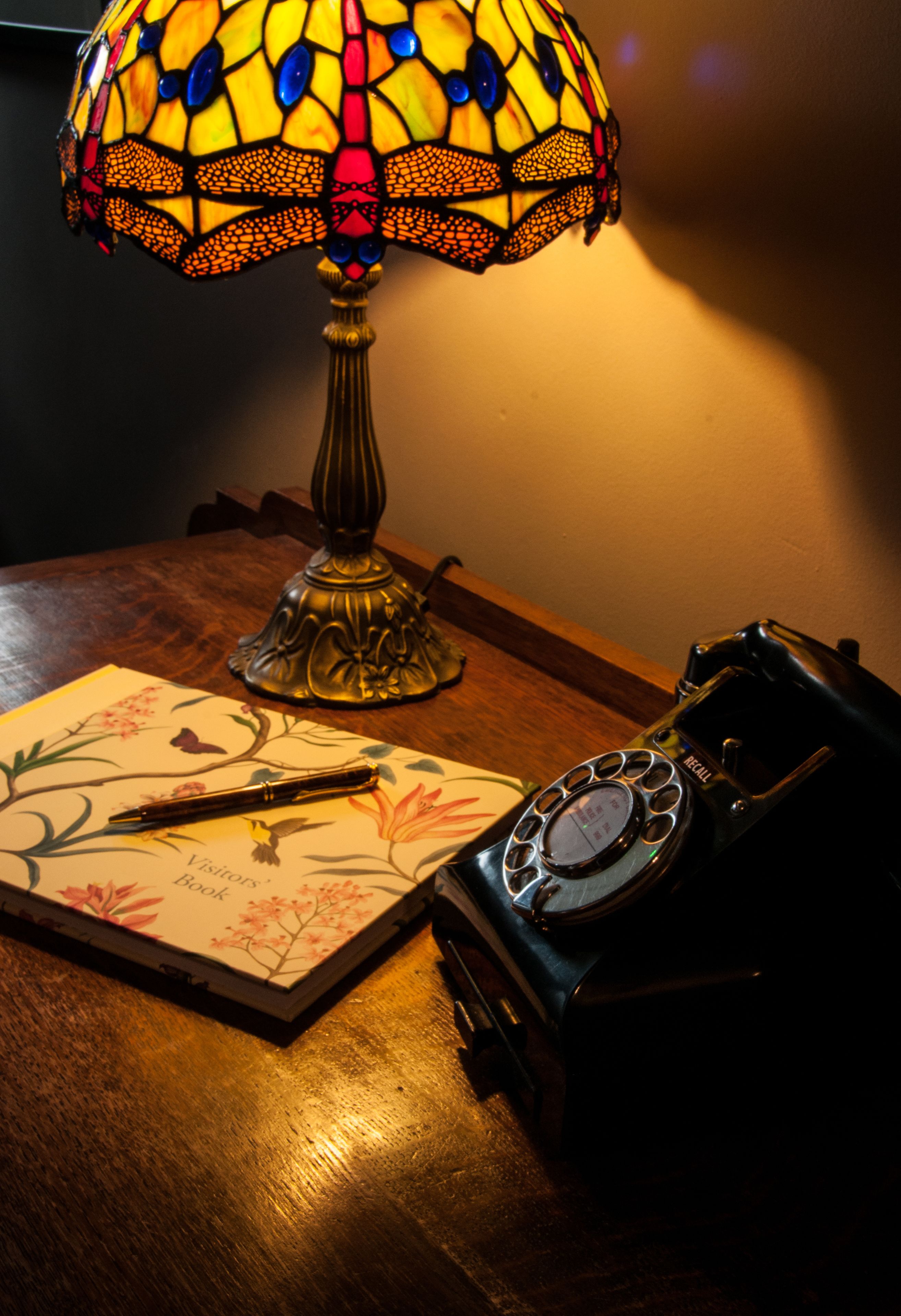 A vintage telephone, a floral book, and a stained glass lamp on a wooden table.