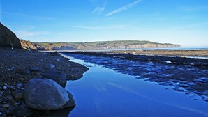 A rocky beach with calm water reflecting the sky, cliffs in the background, and a clear view of the coastline. - Aldersyde Bed and Breakfast (Whitby)