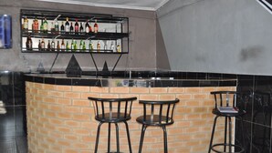 A bar area with a brick counter, three stools, and a shelf with various bottles. - Willu Executive Lodge (Livingstone)