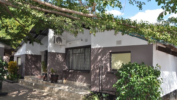 A house with a stone staircase leading to the entrance, surrounded by greenery and a clear sky. - Willu Executive Lodge (Livingstone)